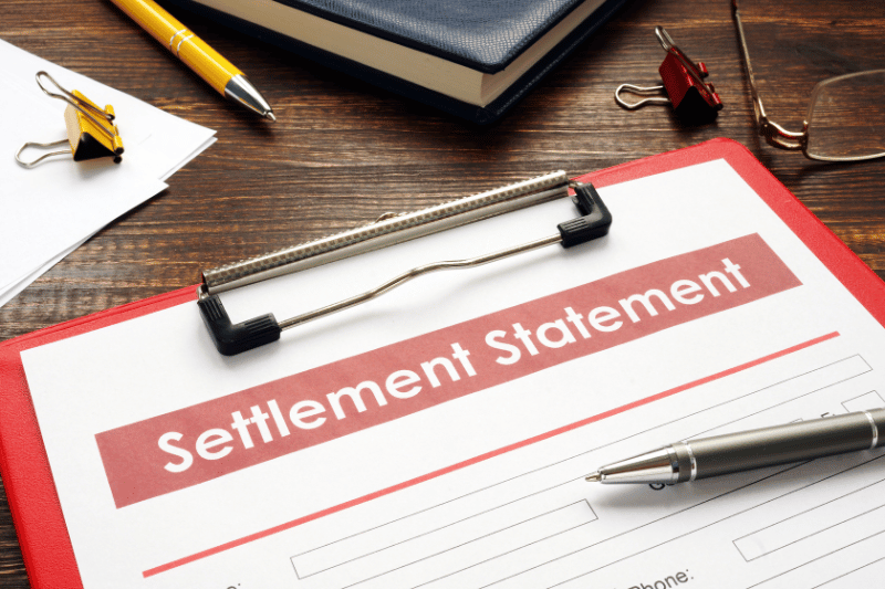 A desk with a settlement statement on a red clipboard, a pen, glasses, and office supplies symbolizing car accident lawyer myrtle beach.