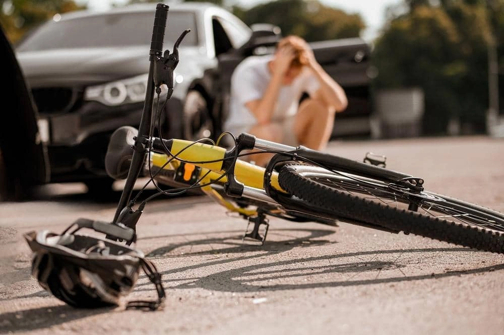 A bicycle lies on its side near a black car, with a person sitting on the ground highlightinh the advantage of hiring bicycle accident lawyer in myrtle beach.