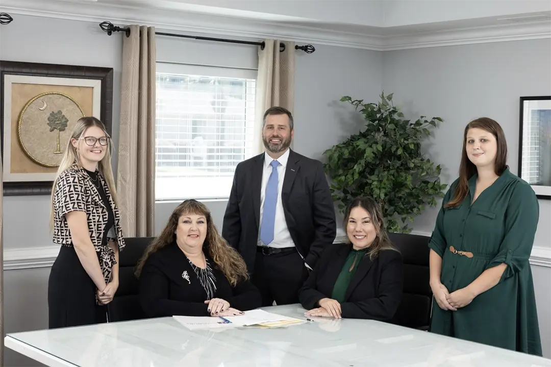 A professional team of five legal staff and a Personal Injury Lawyer in Lake City, SC, posing together in a modern office conference room.